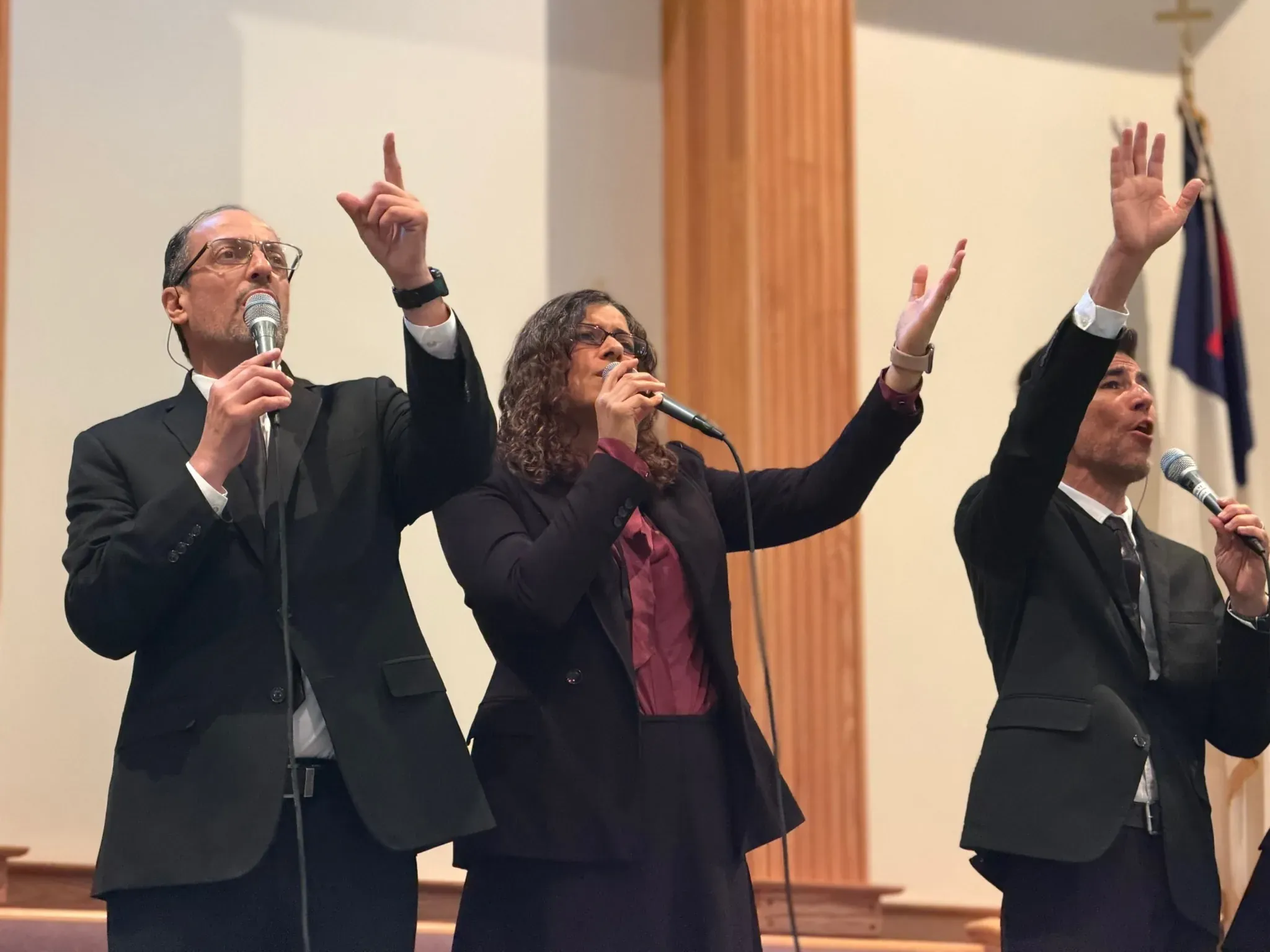 Three Prisma USA singers with their hands raised mid-song